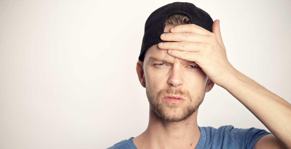 Man in a cap in his thirties holding his head with an annoyed expression