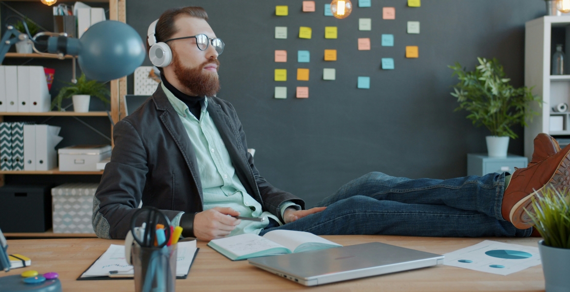Photo of a man wearing headphones, eyes closed, with his feet on his desk.