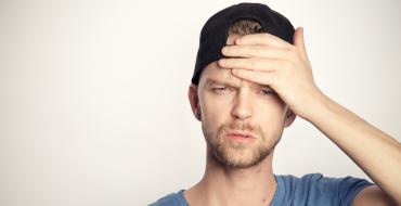 Man in a cap in his thirties holding his head with an annoyed expression