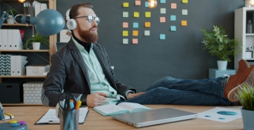 Photo of a man wearing headphones, eyes closed, with his feet on his desk.