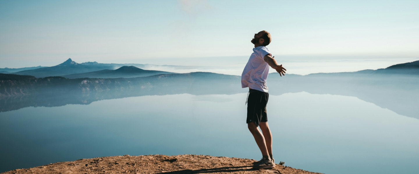 Photo of a man expressing joy and freedom on a hill in front of a mountain lake